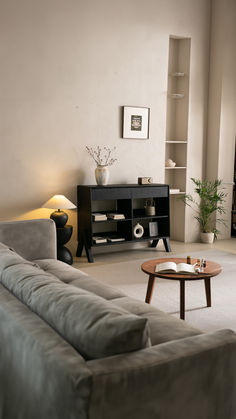 An elegantly minimalist living room featuring a soft colour palette of beige, white, and grey. The room is anchored by a white fireplace, with alcove shelving on either side filled with books and decorative items. A plush beige sofa faces the fireplace, paired with a glass coffee table in the center of the room. On the coffee table, a delicate arrangement of blossoms adds a touch of spring. The design creates a serene and inviting space, showcasing the beauty of minimalist interior design. White And Grey Living Room, Scandinavian Shelves, Grey Living Room, Tranquil Retreat, Design Philosophy, Scandinavian Inspired, Living Room Grey, Clutter Free, Modern Spaces