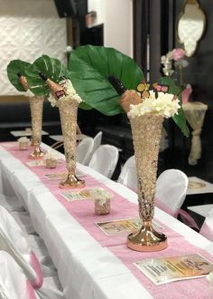 three tall vases filled with flowers and greenery on top of a long table