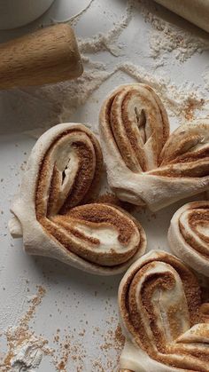 some cinnamon rolls are sitting on a white surface next to a rolling pin and dough