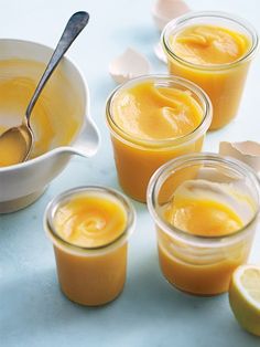 four jars filled with orange curd next to sliced lemons