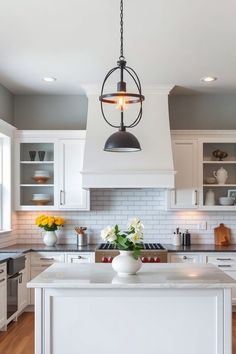 Modern kitchen with white cabinetry, marble countertops, pendant light fixture, and decorative vases on the island and counters. Farmhouse Kitchen Decor Ideas, Trendy Farmhouse, Textured Fabrics