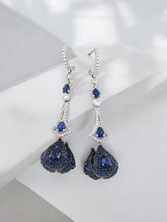 Elevate your jewelry collection with the Lydia 18k White Gold Sapphires Dangle Earrings. Exquisitely crafted in 18k white gold, these luxurious earrings feature natural blue sapphires and are adorned with .73 CTW of sparkling natural diamonds. The striking combination of deep blue sapphires and brilliant diamonds creates a captivating look, perfect for any formal event or a sophisticated evening out. With a graceful 1.5"" dangle design, these earrings offer both elegance and movement, ensuring t Luxury Blue Chandelier Earrings For Formal Occasions, Evening Earrings With Sapphire And Diamond Accents, Evening Sapphire Earrings With Diamond Accents, Sapphire Earrings With Diamond Accents For Evening, Luxury Blue Diamond Drop Earrings, Luxury Blue Pear-shaped Earrings, Blue Teardrop Diamond Earrings, Blue Diamond Drop Earrings With Prong Setting, Luxury Blue Drop Earrings