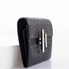 The Cinhetic design, which draws inspiration from moving Kinetic art, is rendered here as a square wallet surrounding an ingenious closure. When locked, the clasp resembles an H for Hermes, but when open, the pieces rotate into a sleek metal line. This extraordinary example is done in Matte Graphite Alligator with Palladium hardware, and features the super useful removable matching Alligator shoulder strap, and a small leather-bound mirror which fits perfectly into one of the wallet’s interior s Luxury Leather Wallets With Silver-tone Hardware, Luxury Leather Wallet With Silver-tone Hardware, Elegant Formal Clutch With Crocodile Pattern, Formal Leather Clutch With Crocodile Pattern, Luxury Crocodile Pattern Business Wallets, Luxury Crocodile Pattern Wallet For Business, Luxury Crocodile Pattern Wallets For Business, Luxury Wallets With Crocodile Pattern For Business, Elegant Crocodile Pattern Formal Wallets