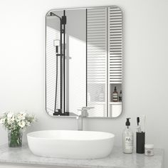 a bathroom sink sitting under a mirror next to a vase with white flowers in it