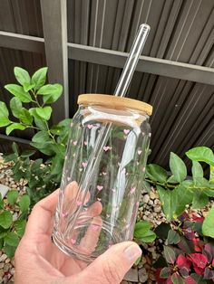 a hand holding a clear glass with pink flowers on it and a straw in the top