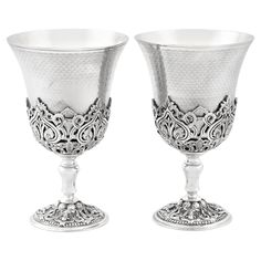 two silver goblets sitting next to each other on a white surface with an intricate design