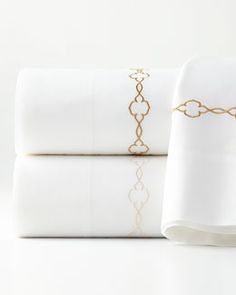 two white sheets with gold trim on them and one has a pillow case in the middle