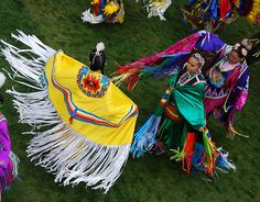 several people dressed in colorful clothing and headdress are dancing on the grass together