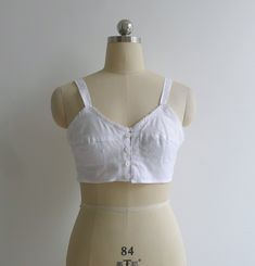 "Brand new vintage deadstock from the 1970's. Soviet era white longline bra top in 100% cotton. Features darted bra cups with circle stitching to the bottom half, slim shoulder straps & a sweet picot trim to the bustline. Closes with a column of buttons to the center front. Could be worn as an undergarment, or even as a cropped camisole top. 100% cotton takes dye well & could be a fun project too! Check out other brassieres in the shop - www.etsy.com/shop/fivestonesvintage?section_id=100 Vintage Bra, Cotton Bra, Bra Items, Cotton Camisole, Cropped Camisole, Vintage Nightgown, Cotton Bras, Handmade Wardrobe, Longline Bra