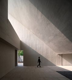 a person walking in an empty room with concrete walls and flooring on both sides