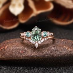 an oval cut green and white diamond ring on top of a rock with flowers in the background