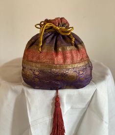 "A Purple/coral/gold vintage silk wedding sari (circa1950's) was used to create this beautiful drawstring handbag that is lined with silk charmeuse and finished with a 4\" Spanish tassel. It is a one of a kind and was made by me in the early 2000's. This beauty can also be used for storing jewelry, or stuffed and displayed amongst your fabulous collections! There is a little bit of foxing on the gold stripe at the mid point of the handbag. This is minor, however, important to let you know condit Drawstring Handbag, Storing Jewelry, Purple Coral, Wedding Sari, Vintage Sari, Coral And Gold, Evening Handbag, Silk Wedding, Vintage Saris