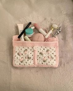 a pink crocheted purse with cosmetics and other items in it on a bed