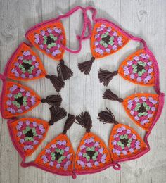 an orange and pink crocheted doily with tassels on top of it