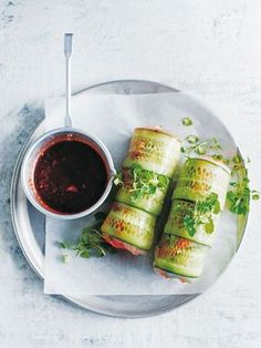 a plate topped with cucumber rolls next to a bowl of ketchup