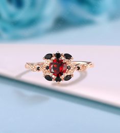 a red and black diamond ring sitting on top of a white table next to blue roses