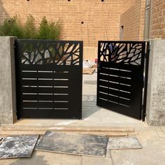 two black gates are open in front of a brick wall and concrete slabs on the ground