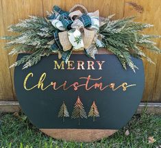 a merry christmas sign with evergreens and burlocks on the bottom, sitting in front of a wooden door