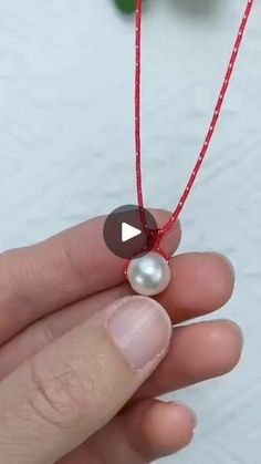 a person holding a red string with a white pearl on it