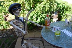 a skeleton sitting at an outdoor table with cards on it