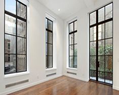 an empty room with wood floors and three windows in the corner, all white walls