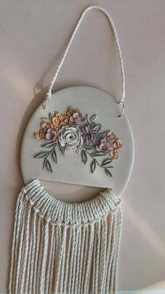 a white ceramic wall hanging with flowers on it's side and tassels around the edge