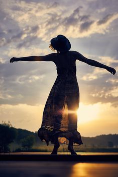 a woman standing in front of the sun with her arms outstretched