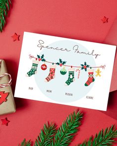 a christmas card with stockings hanging on a clothes line and presents next to it, surrounded by evergreen branches