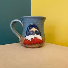 a blue and red bird mug sitting on top of a counter next to a yellow wall