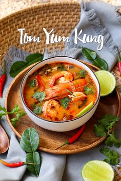 a bowl of soup with shrimp, lime and cilantro on a wooden plate