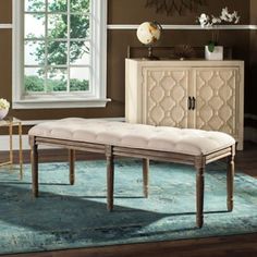 a white bench sitting on top of a rug next to a dresser and window in a living room