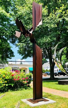 a metal sculpture in the middle of a grassy area with trees and flowers behind it