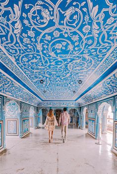 two people are walking in an ornately painted room with blue walls and ceiling tiles