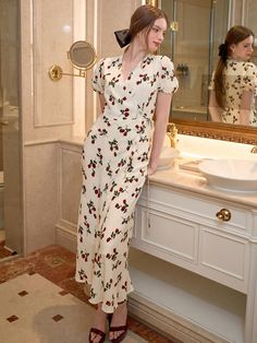 a woman standing in front of a bathroom mirror wearing a dress with flowers on it