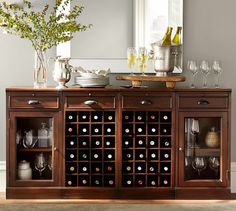 a buffet table with wine bottles and glasses on it in front of a large mirror