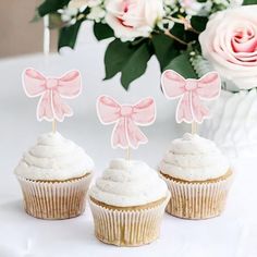 three cupcakes with pink bows are on a table next to some white flowers