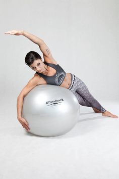 a woman is sitting on an exercise ball and stretching with her arms out to the side