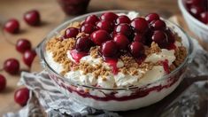 a dessert with cherries and whipped cream in a glass bowl on a wooden table