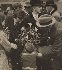 an old black and white photo of a man handing flowers to a child