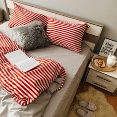 a bed with red and white striped sheets, pillows and blankets on top of it