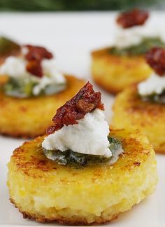 small appetizers are arranged on a white plate with greens and cream toppings