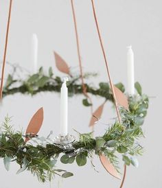 a wreath with candles hanging from it and greenery on the bottom, surrounded by leaves