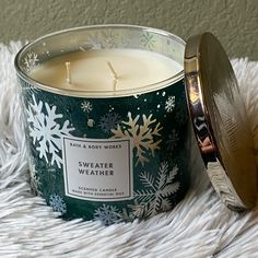 a candle sitting on top of a white blanket next to a metal container filled with snowflakes