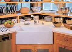 a white kitchen sink sitting under a window next to wooden shelves filled with dishes and bowls