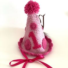 a crocheted hat with a pink ribbon around it and the number one on top