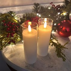 two lit candles sitting on top of a table next to christmas decorations and greenery