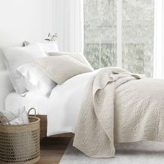 a bed with white linens and pillows in a bedroom next to a basket on the floor