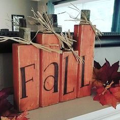 a wooden block with the word fall written on it next to some fake leaves and twine