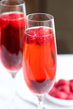 two wine glasses filled with red liquid and raspberries