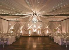 a banquet hall decorated with white draping and chandelier draped over the tables